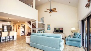 A spacious living area with a high ceiling, a ceiling fan, a staircase, a kitchen, and a dining area. - Pet friendy 3-BR retreat with gulf views & crows nest balcony - Signal Inn 18 (Sanibel)
