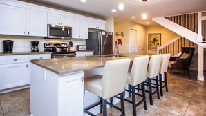 A modern kitchen with white cabinets, stainless steel appliances, a central island with bar stools, and a staircase leading to a living area. - Pet friendy 3-BR retreat with gulf views & crows nest balcony - Signal Inn 18 (Sanibel)