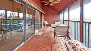 A wooden deck with glass doors leading to a patio area, furnished with a table and chairs, and a ceiling fan. - Pet friendy 3-BR retreat with gulf views & crows nest balcony - Signal Inn 18 (Sanibel)