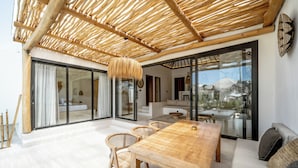 A spacious living area with a wooden dining table and chairs, a sofa, and a large glass door leading to an outdoor patio. - Villa Rosado Canggu (Canggu)