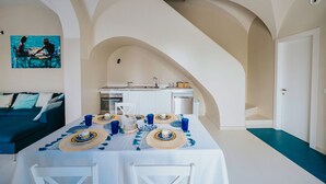 A dining area with a white table set for four, a kitchen in the background, and a blue accent wall. - Villa Matilde by Elite Villas (Capri)