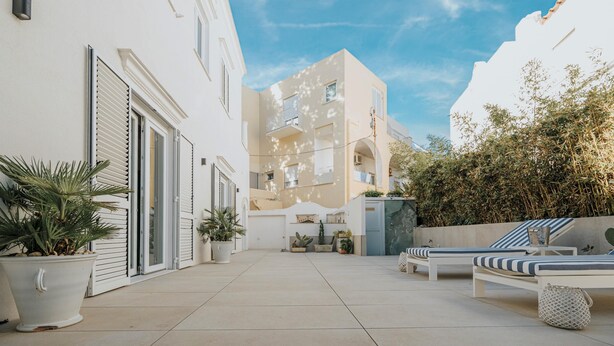 A courtyard with a white building, potted plants, and a lounge area with striped cushions. - Villa Matilde by Elite Villas (Capri)