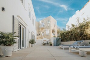 A courtyard with a white building, potted plants, and a lounge area with striped cushions.