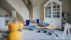 A dining table with a white tablecloth, blue and white plates, and a yellow fruit bowl. A white cabinet with blue dishes is in the background. - Villa Matilde by Elite Villas (Capri)