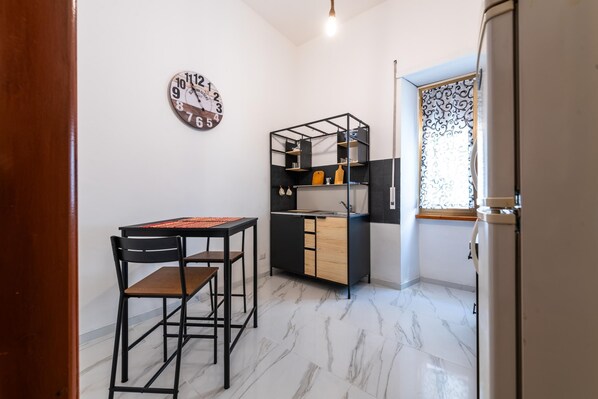 A compact kitchen with a built-in sink, a small dining area with a table and chairs, and a decorative wall clock.