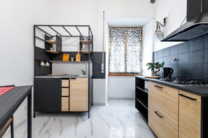 A modern kitchen with a central island, black and white tiled backsplash, and a window with patterned curtains.