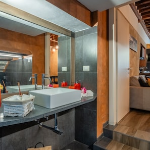 A modern bathroom with a large mirror, a white sink, and a wooden floor.