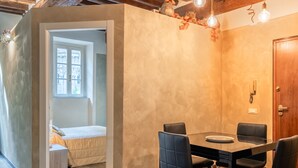 Zona pranzo con tavolo in legno e quattro sedie, soffitto in legno con travi a vista e una porta con un telefono appeso al muro.