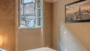 Una camera da letto con un letto grande, una finestra vista su un edificio storico e un dipinto che raffigura un panorama urbano.