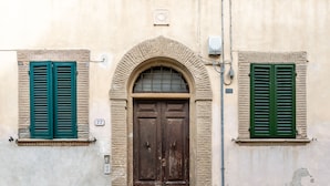 Un edificio con un'ampia porta ad arco centrale, persiane verdi e gradini in pietra che conducono all'ingresso.