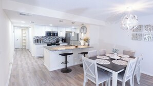 Une cuisine moderne avec des meubles blancs, un îlot central et un coin repas comprenant une table et des chaises.
