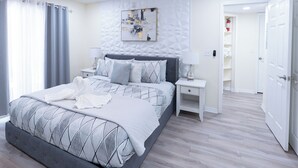 Une chambre à coucher moderne, comprenant un lit, des tables de chevet, une table de nuit, une œuvre d’art accrochée au mur et un placard.