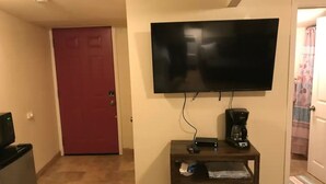 Habitación de hotel con televisor montado en la pared, cafetera sobre una mesita y una puerta roja.