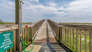 Una passerella in legno che conduce a una piscina, con un cartello che invita a rimuovere la sabbia prima di entrare.