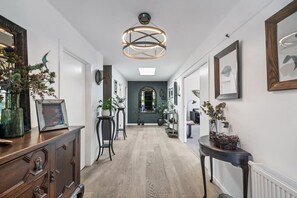 A hallway with a wooden floor, a ceiling light fixture, and framed artwork on the walls.