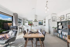 A modern kitchen with a dining area, a bookshelf, and a view of the outdoors.