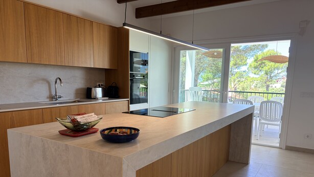 Een moderne keuken met houten kastjes, een groot eiland, een ingebouwde oven en uitzicht op het buitenbalkon.