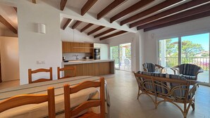 Een moderne keuken met houten balken, een eethoek met rieten stoelen, en een balkon met uitzicht.