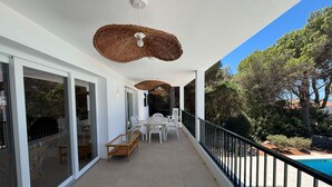 Een balkon met een zwembad, rieten plafondlampen en een eethoek met stoelen.