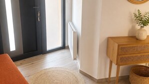 Une pièce dotée d’une grande porte-fenêtre coulissante, d’un miroir rond, d’une console en bois, d’un tapis tissé et d’un pouf orange.