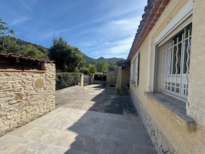 A stone building with a tiled patio, a window with metal bars, and a mountain in the background.