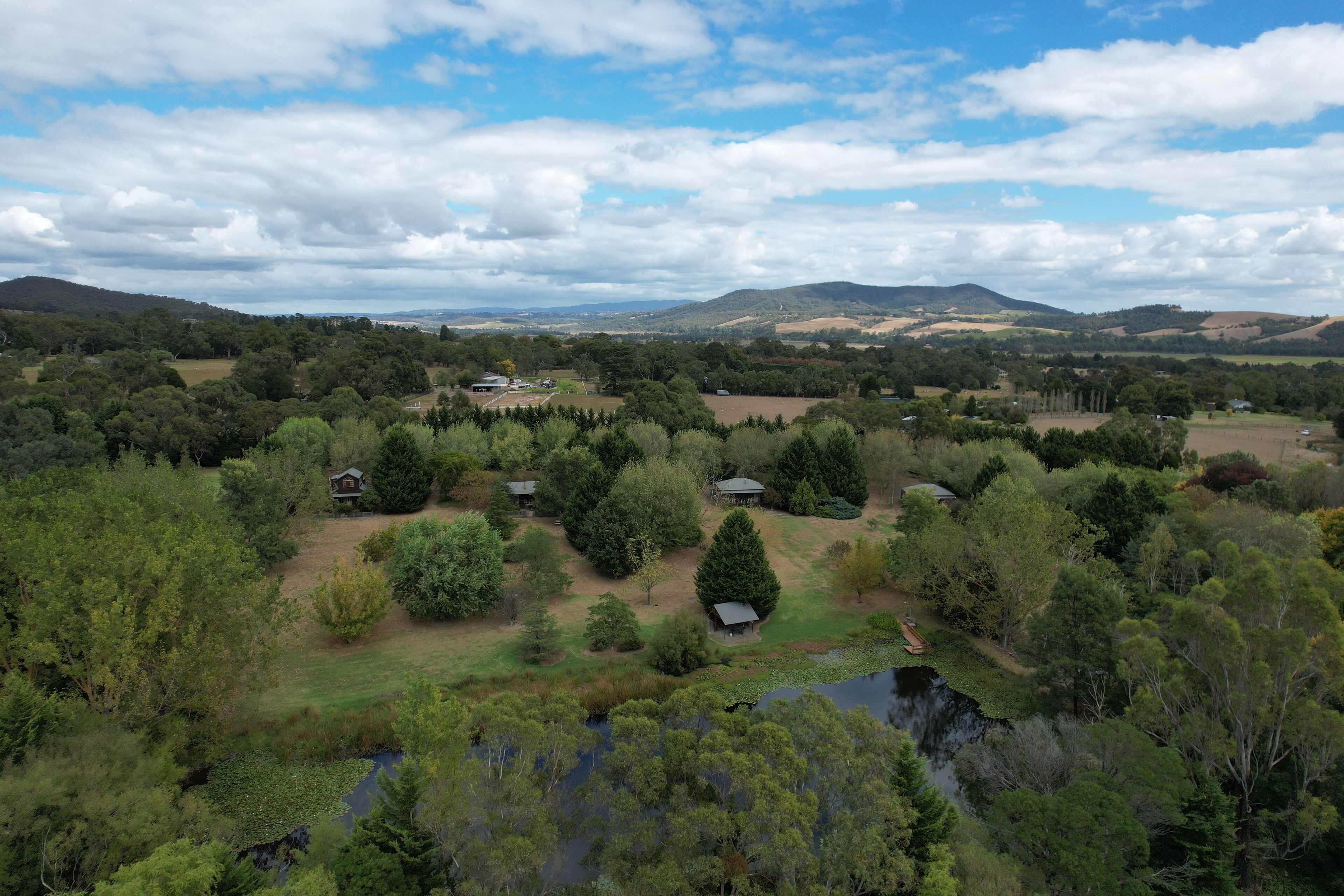 A rural landscape with multiple houses surrounded by dense vegetation and hills in the background.