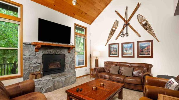 A cozy living room with a stone fireplace, leather sofas, a coffee table, and a mounted television. - Fantastic Golf and Ski Retreat Surrounded by Trees, Private Hot Tub, Game Room, BBQ (Mount Hood Village)