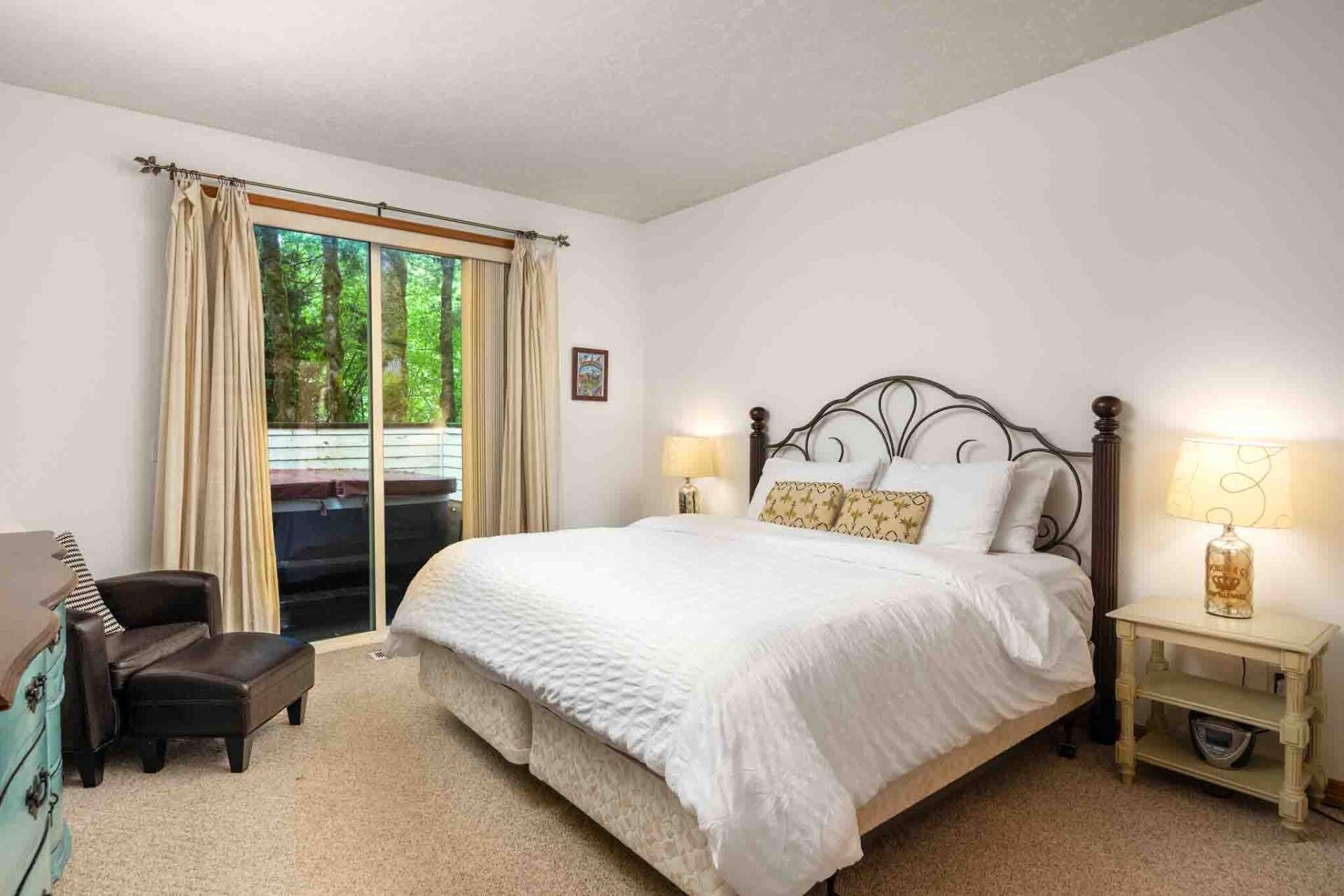 A bedroom with a large bed, a chair, a nightstand, and a window with curtains.