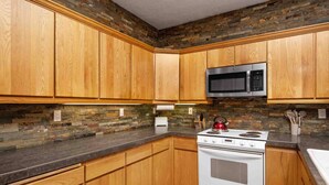 A kitchen with wooden cabinets, a stainless steel microwave, a white stove, and a stone backsplash. - Fantastic Golf and Ski Retreat Surrounded by Trees, Private Hot Tub, Game Room, BBQ (Mount Hood Village)
