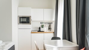 Een kleine keuken met een magnetron, koffiezetapparaat en keukengerei dat aan de muur hangt.
