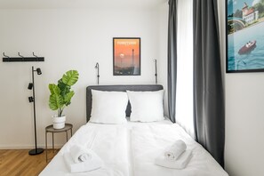 Ein ordentlich bezogenes Bett mit weißen Bettwäsche, ein Blumentopf und ein gerahmtes Stadtbild an der Wand.