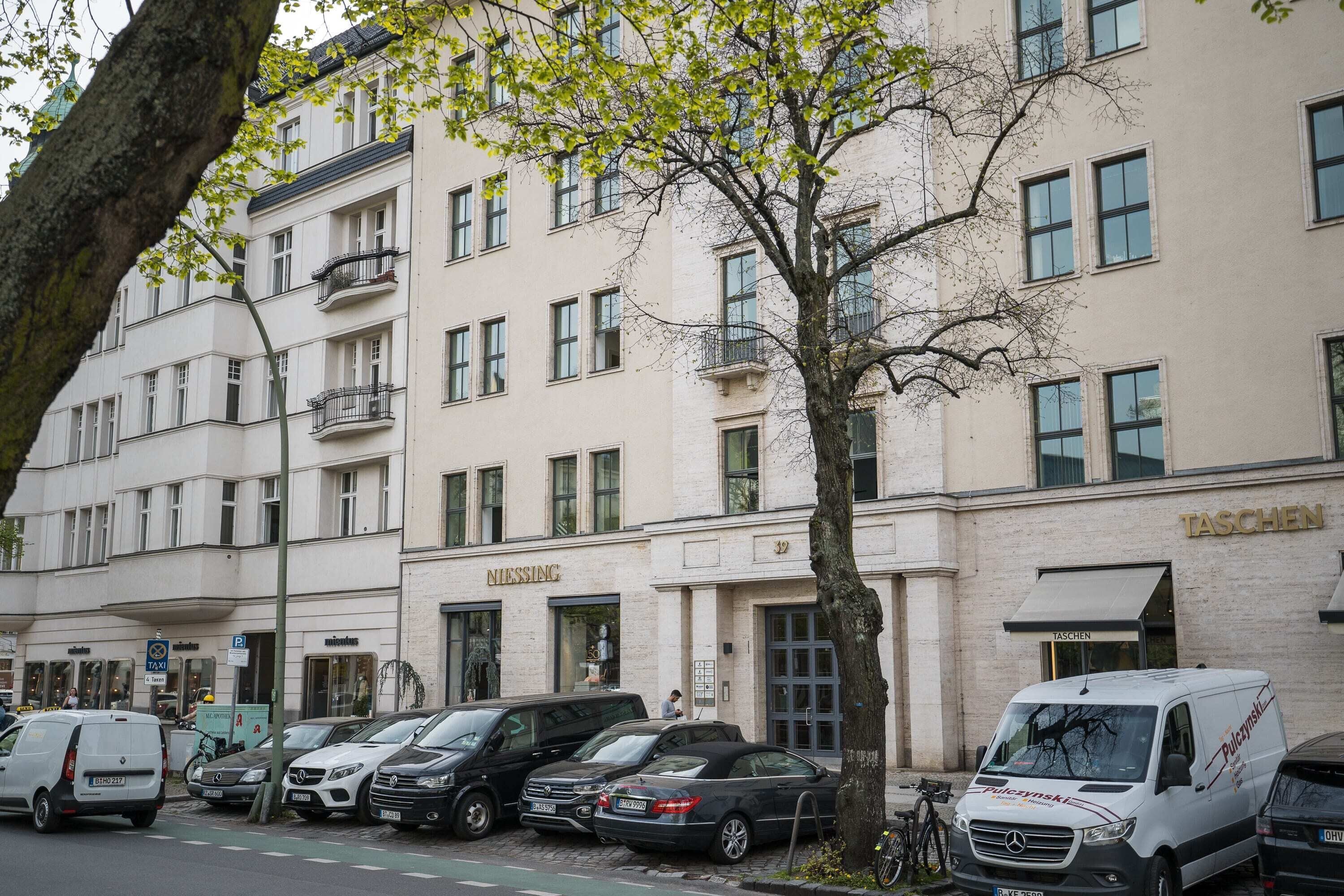 A row of parked cars and a white van in front of a building with a sign reading "TASCHEN".