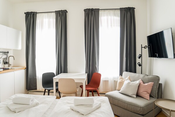 A hotel room with a bed, a desk, a chair, a sofa, and a TV.