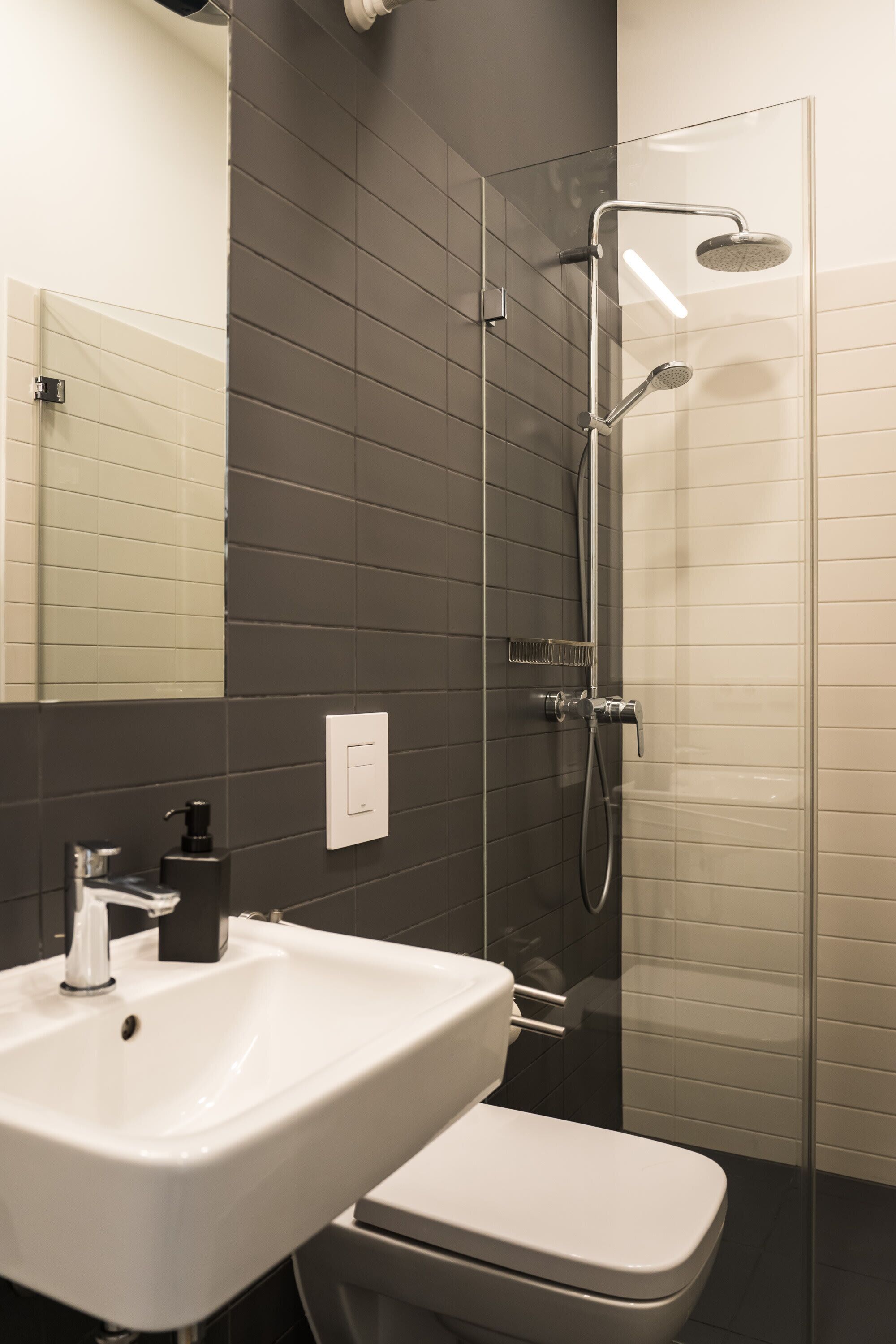 Une salle de bain moderne avec un lavabo blanc, des toilettes et une douche séparée par une paroi de verre.