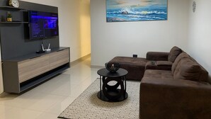 Una sala de estar moderna con un televisor de pantalla plana, un sofá marrón, un tapete estampado y un cuadro de una vista marina.