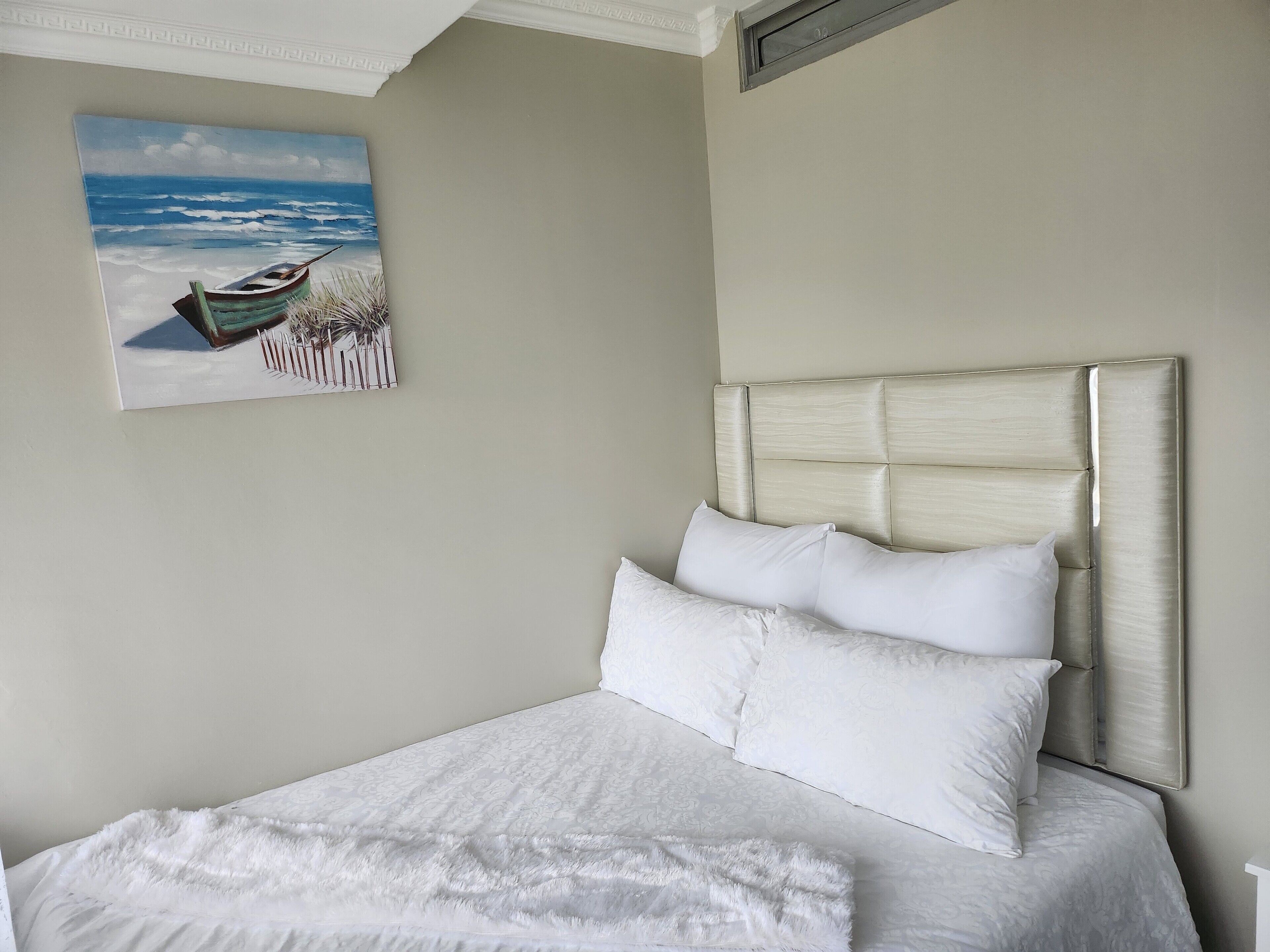 Ein ordentlich bezogenes Bett mit weißen Leinen und einem Kopfteil, ein Gemälde eines Bootes am Strand und eine schlichte Wand.