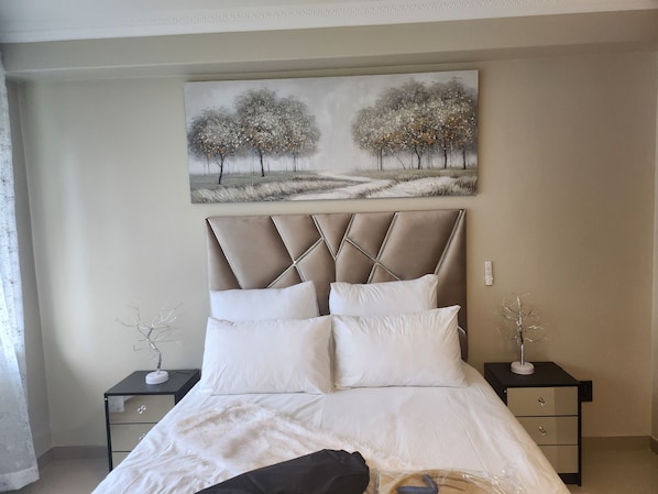 A bedroom with a bed, two nightstands, a painting, and a window with a curtain.