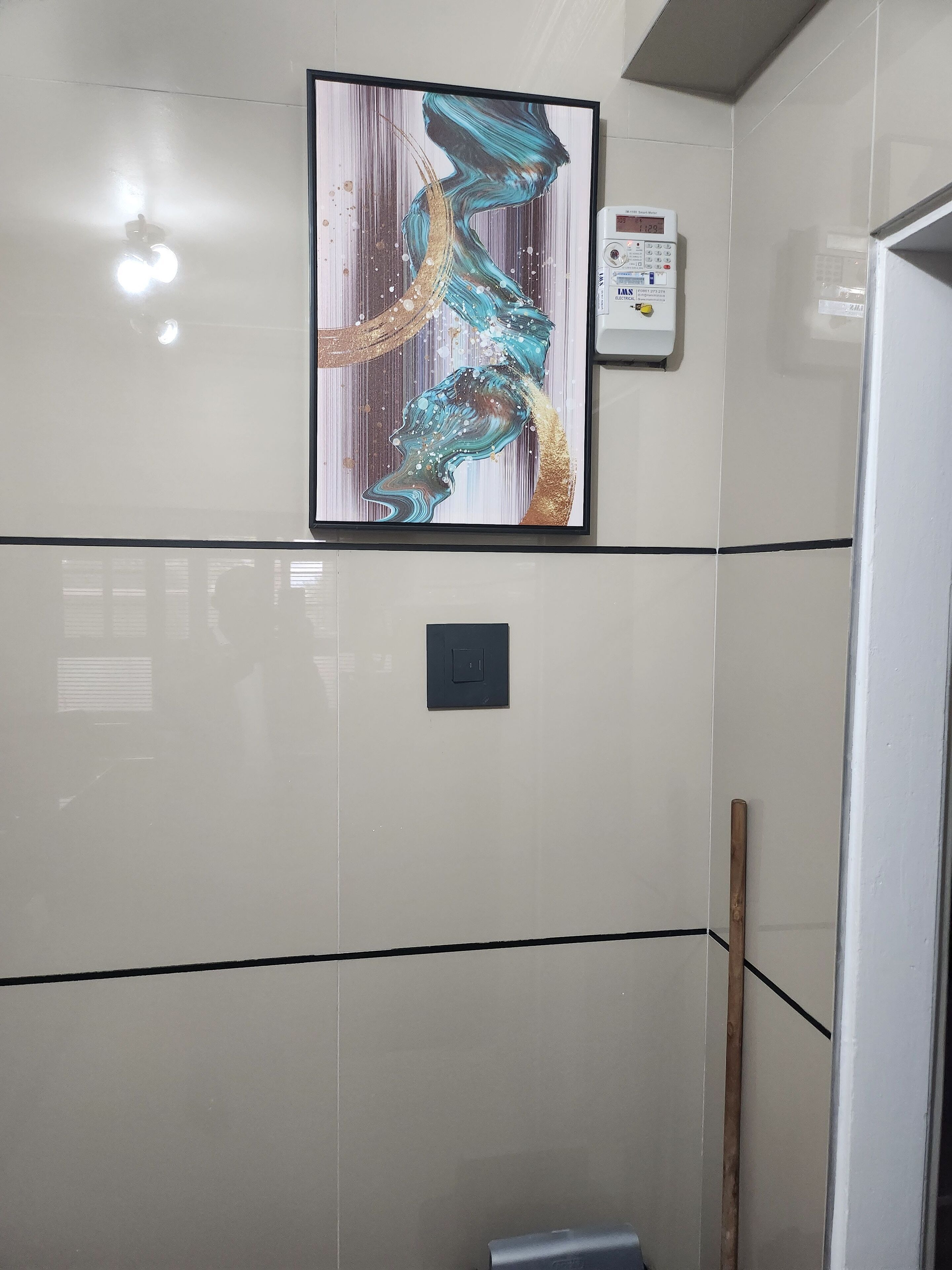 Ein Badezimmer mit einem großen abstrakten Gemälde, einem digitalen Thermostat und einem Holzstab, der an der Wand lehnt.