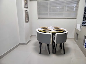 A small dining area with a round table, four chairs, and a window with blinds.