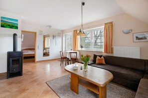 A living room with a sofa, a wooden coffee table, a dining table with chairs, a fireplace, and a window with curtains.