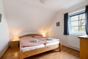 Ein Schlafzimmer mit einem hölzernen Bett, Nachttischlampen, einem Fenster mit Vorhängen und einer Heizung.