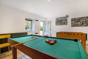 Una mesa de billar con bolas, una mesa de fútbol de mesa y un banco.