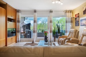 Una sala de estar con un sofá, una mesa de centro de vidrio, un televisor y vistas al verdor exterior.