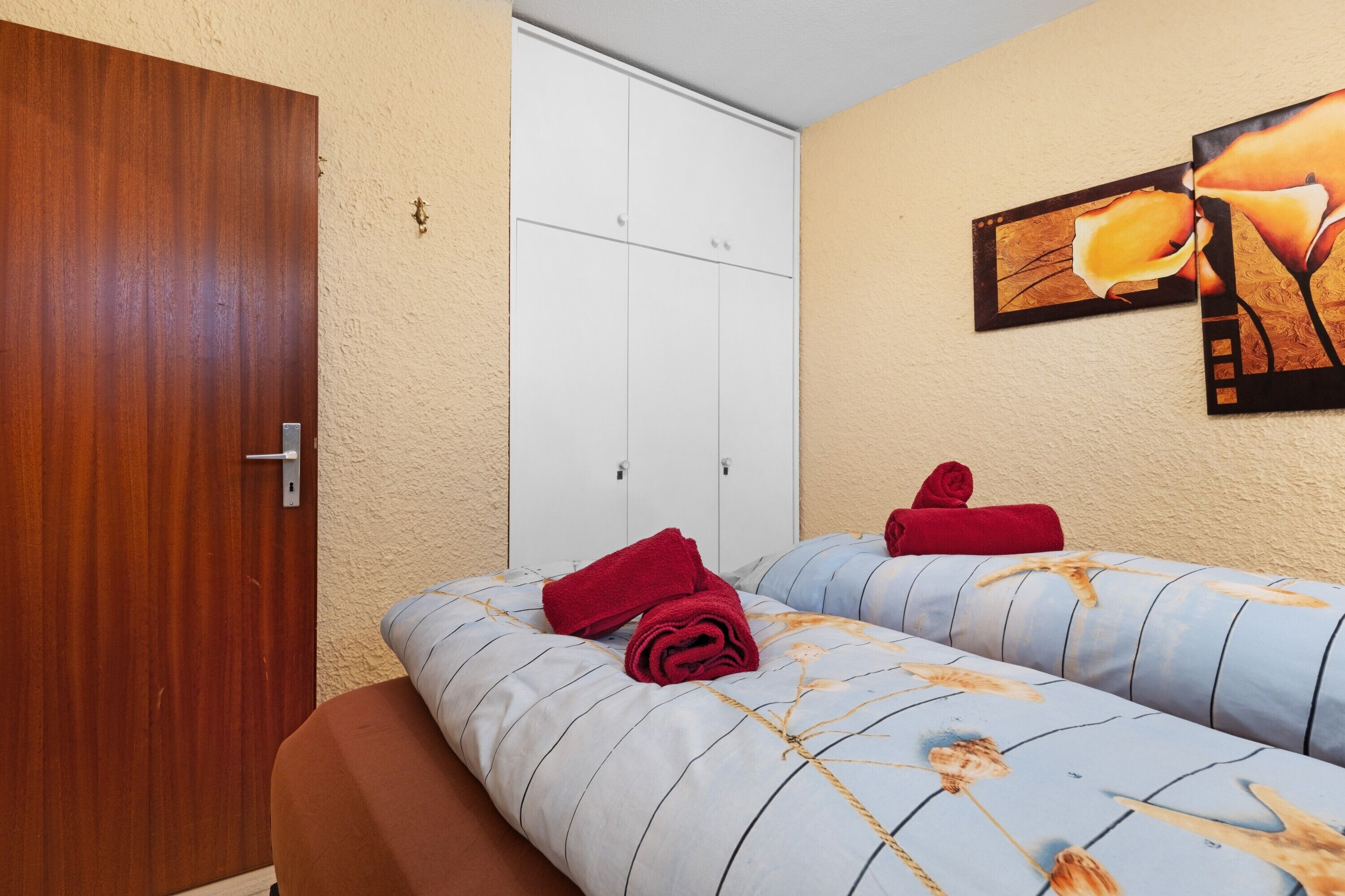 A hotel room with two beds, a wooden door, a white wardrobe, and a wall-mounted artwork.