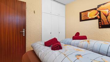 A hotel room with two beds, a wooden door, a white wardrobe, and a wall-mounted artwork.