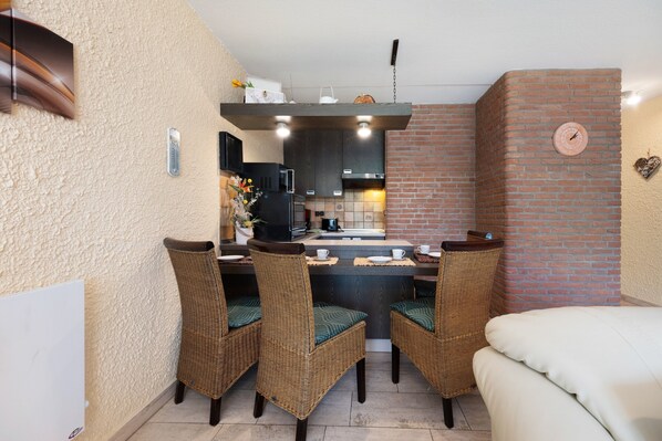 Una cocina compacta con pared de ladrillo, un rincón de comedor con sillas de mimbre y una cama.
