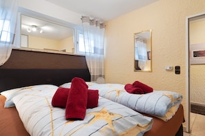 A hotel room with a bed, a large mirror, a wall-mounted light, and a door. - Apartment 'Seeadler' with Balcony and Wi-Fi (Butjadingen)