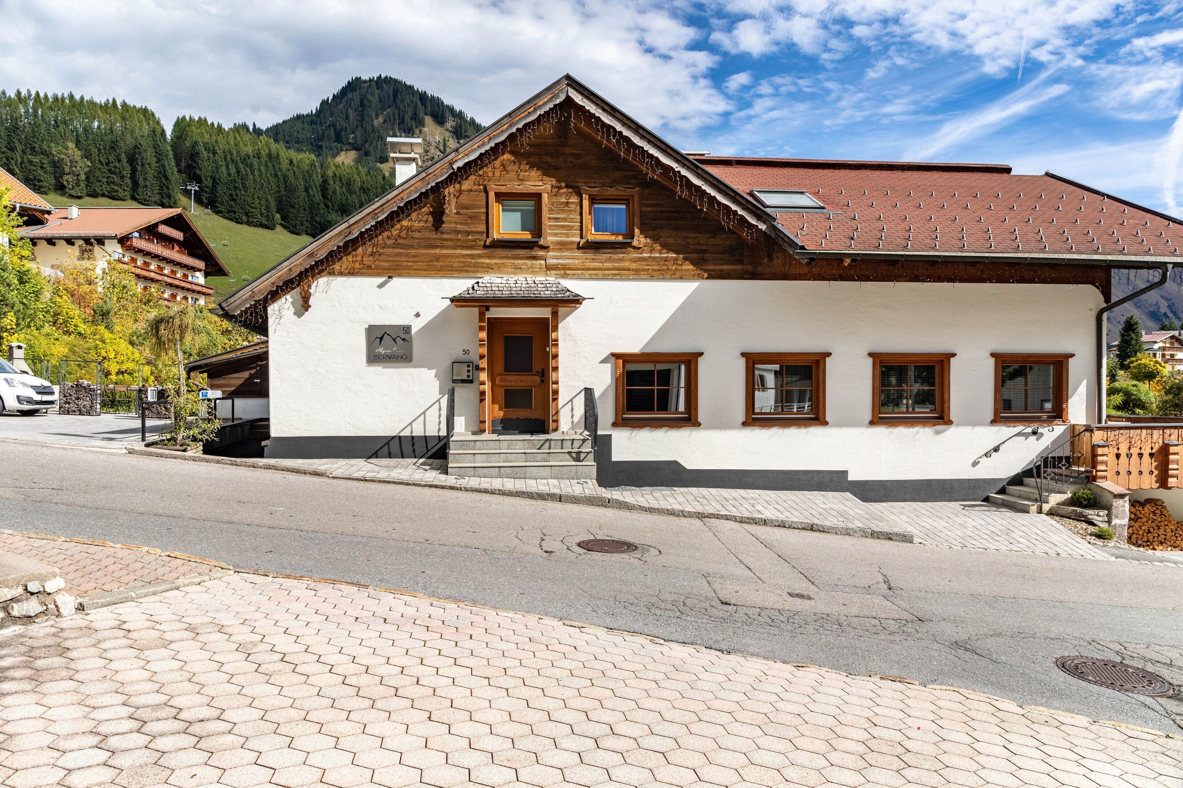 Un chalet traditionnel en bois, avec une façade blanche, un escalier en bois et une vue sur les montagnes en arrière-plan.