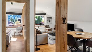 A modern interior with a wooden dining table, a sofa, a TV, and a view of the outdoors.
