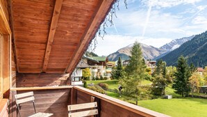 A wooden balcony with a view of a mountain landscape, a table, and two chairs.